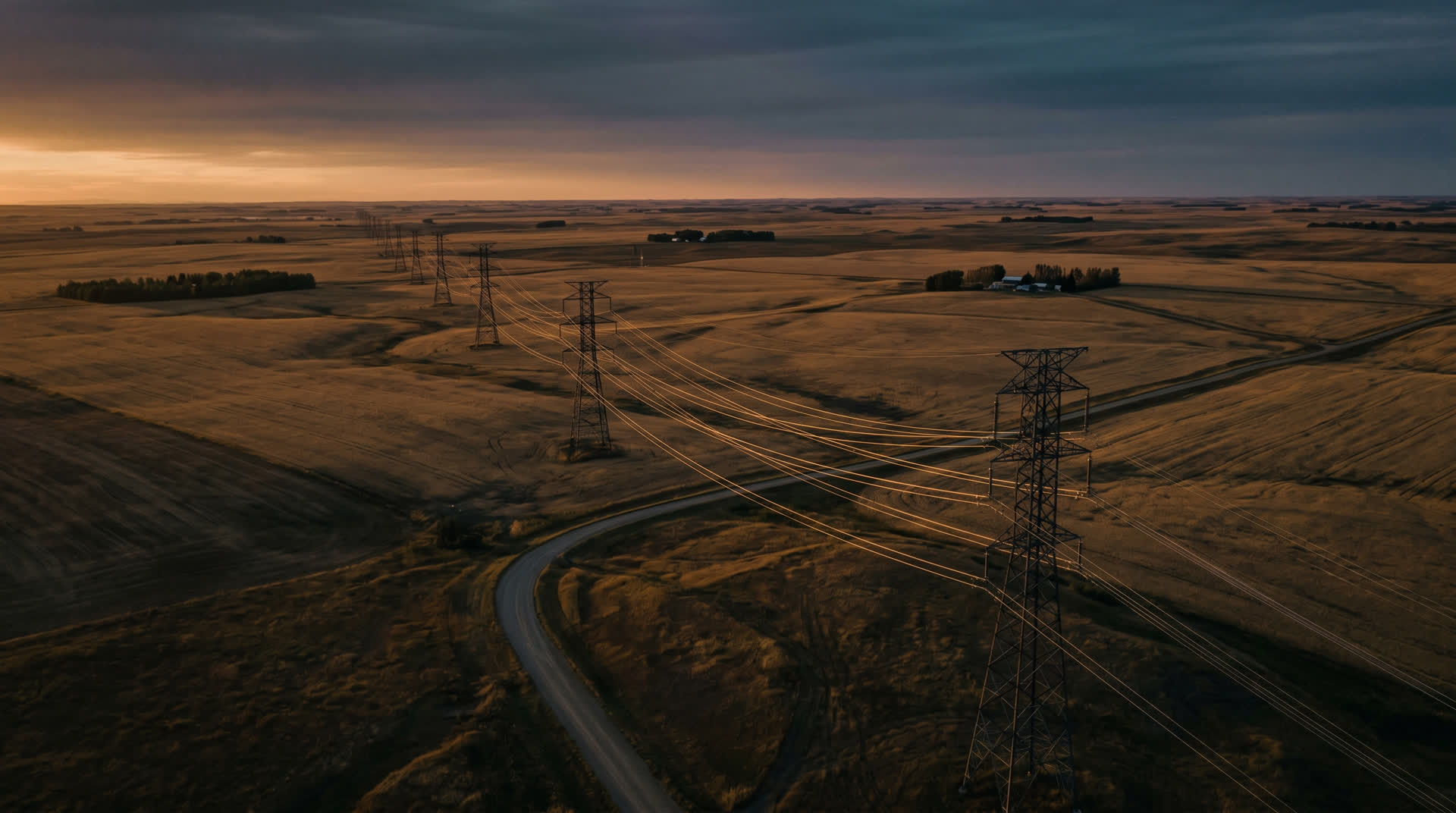 High-voltage transmission lines crossing Alberta prairie at golden hour.